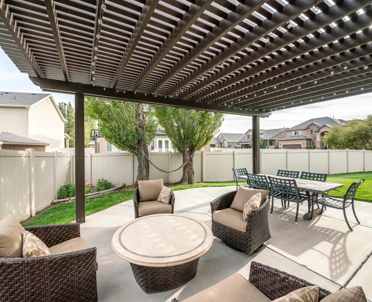 Dark lattice pergola shading a concrete patio with wicker chairs and a dining set