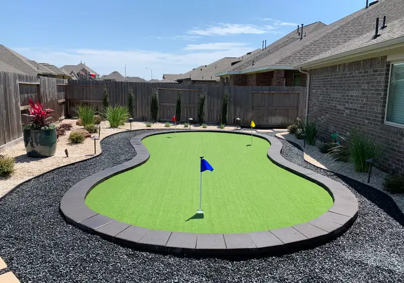 Kidney-shaped artificial putting green with flags and gray curb border in a Houston backyard