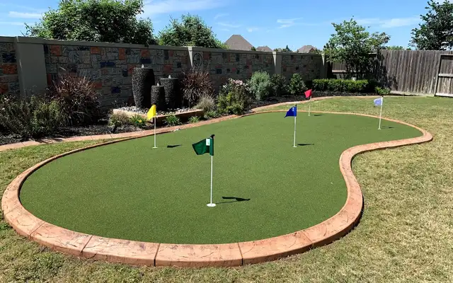 Artificial turf putting green with flags and stamped concrete curb edging in a backyard