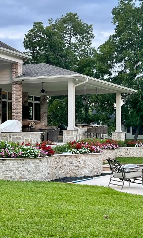 Covered patio with stacked stone planter walls full of red and pink flowers
