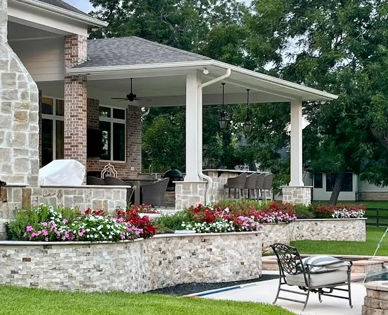 Stacked stone planter beds full of red and pink flowers beside a covered patio