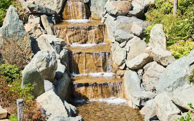 Multi-tiered natural boulder waterfall cascading into a shallow stream in a garden
