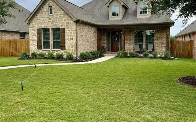 Front lawn of a stone and brick house watered by several pop-up sprinklers