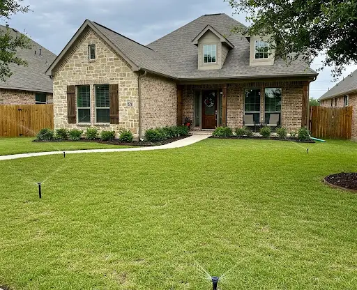 Stone and brick house with a front lawn being watered by pop-up sprinklers