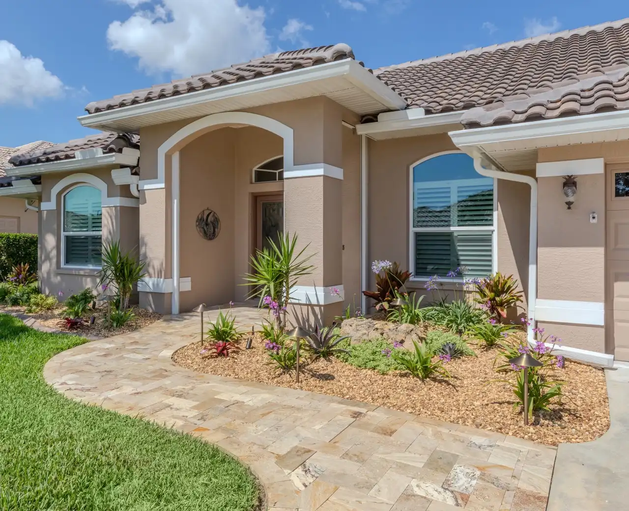 Stucco home with a tile roof, travertine paver walkway and tropical planting beds