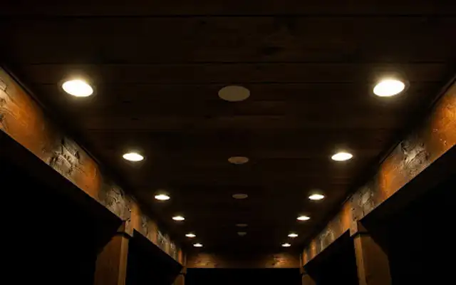 Recessed lights glowing in a dark stained wood ceiling with beams