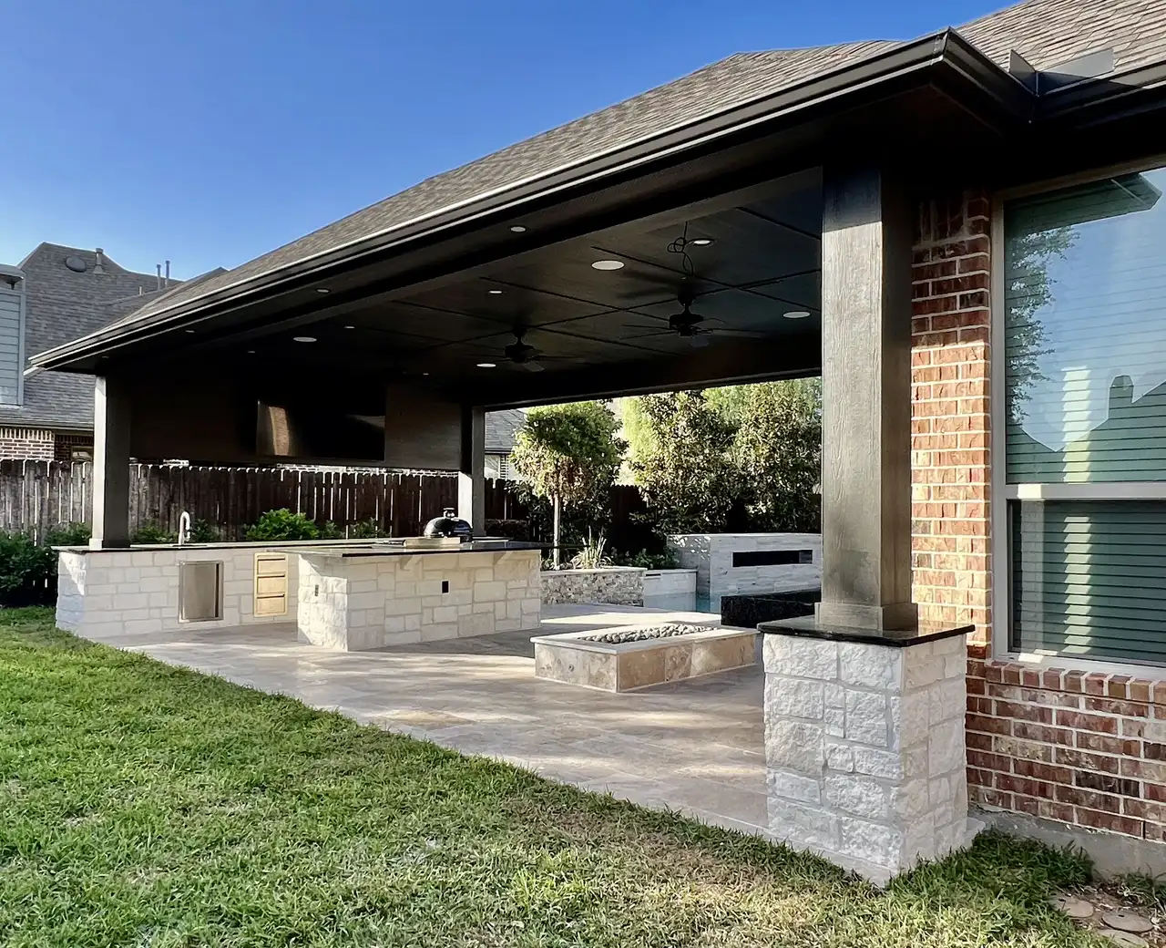 Long patio cover with white stone columns, outdoor kitchen, fire feature and travertine floor, built by HLI