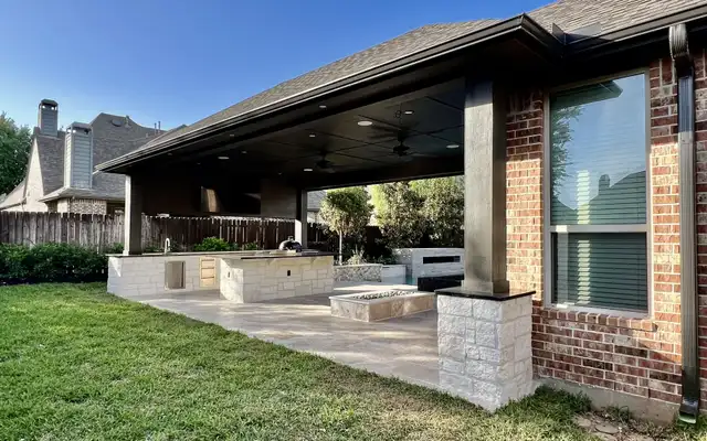 Long dark-roof patio cover on white stone columns over an outdoor kitchen and travertine
