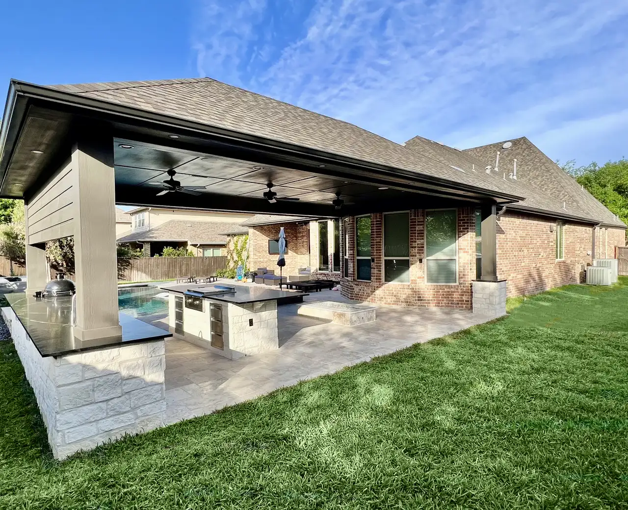 Patio cover with a stone outdoor kitchen island overlooking a pool and large lawn