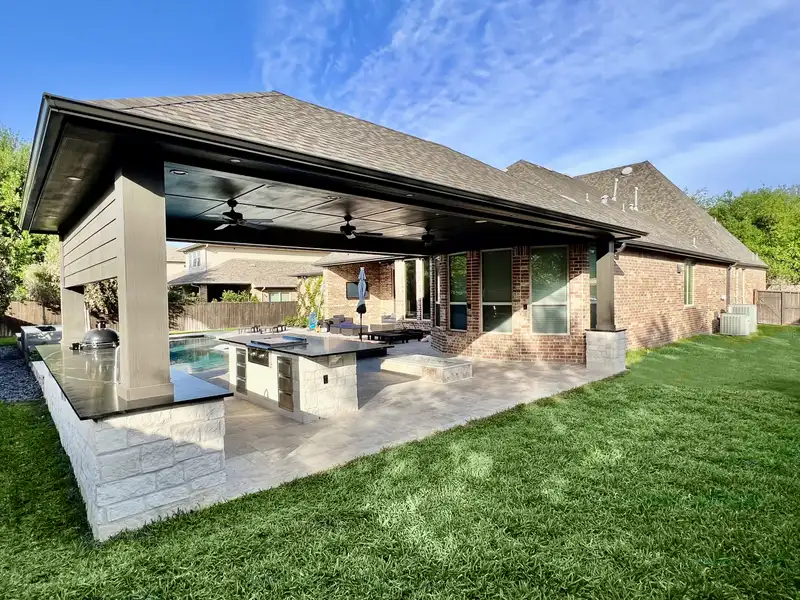 Shingle roof patio cover with stone column and outdoor kitchen island overlooking a pool
