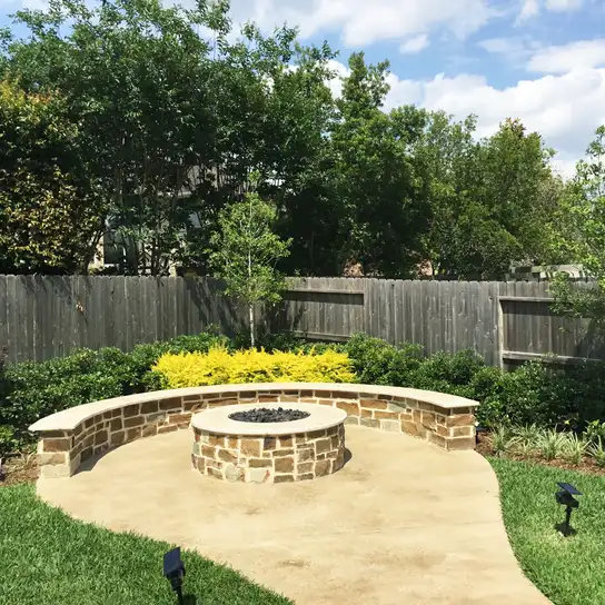 Round stone fire pit and curved seat wall on a concrete patio with landscape lights