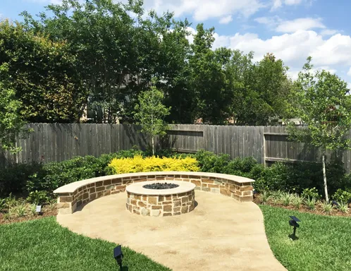 Round stone fire pit and curved seat wall on a concrete patio with landscape lights