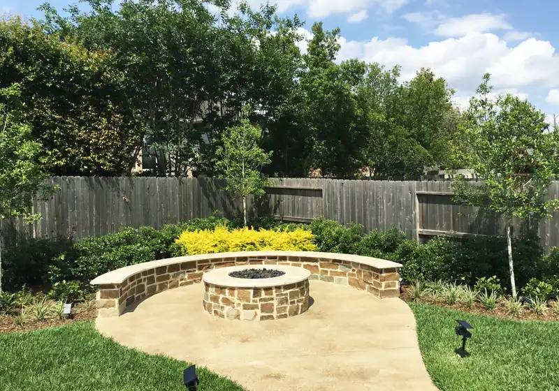 Round stone fire pit and curved seat wall on a concrete patio with landscape lights
