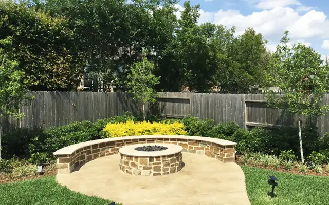 Round flagstone fire pit with curved seat wall on a concrete patio, built by HLI