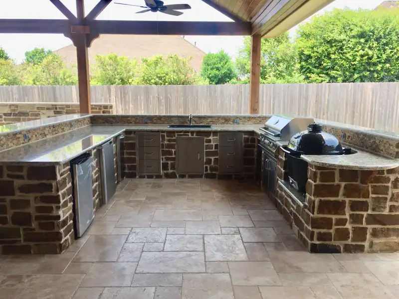 U-shaped stone outdoor kitchen with granite counters, stainless doors and a kamado grill