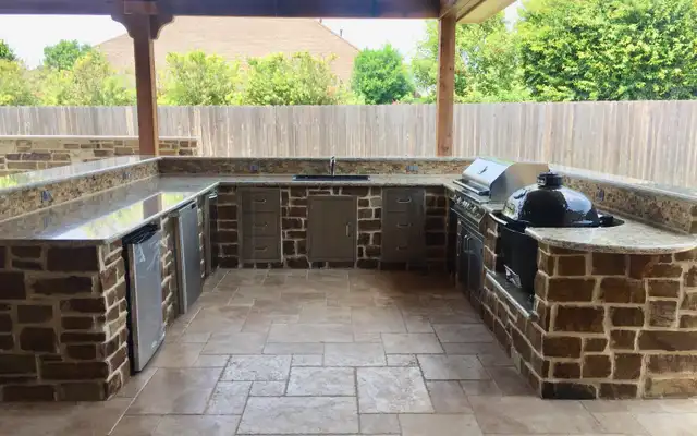 U-shaped stone outdoor kitchen with granite counters, stainless doors and a kamado grill
