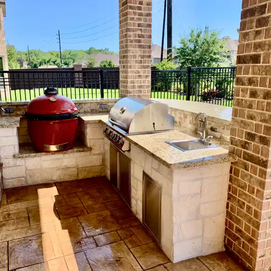 Limestone outdoor grill station with red kamado cooker, stainless grill and sink