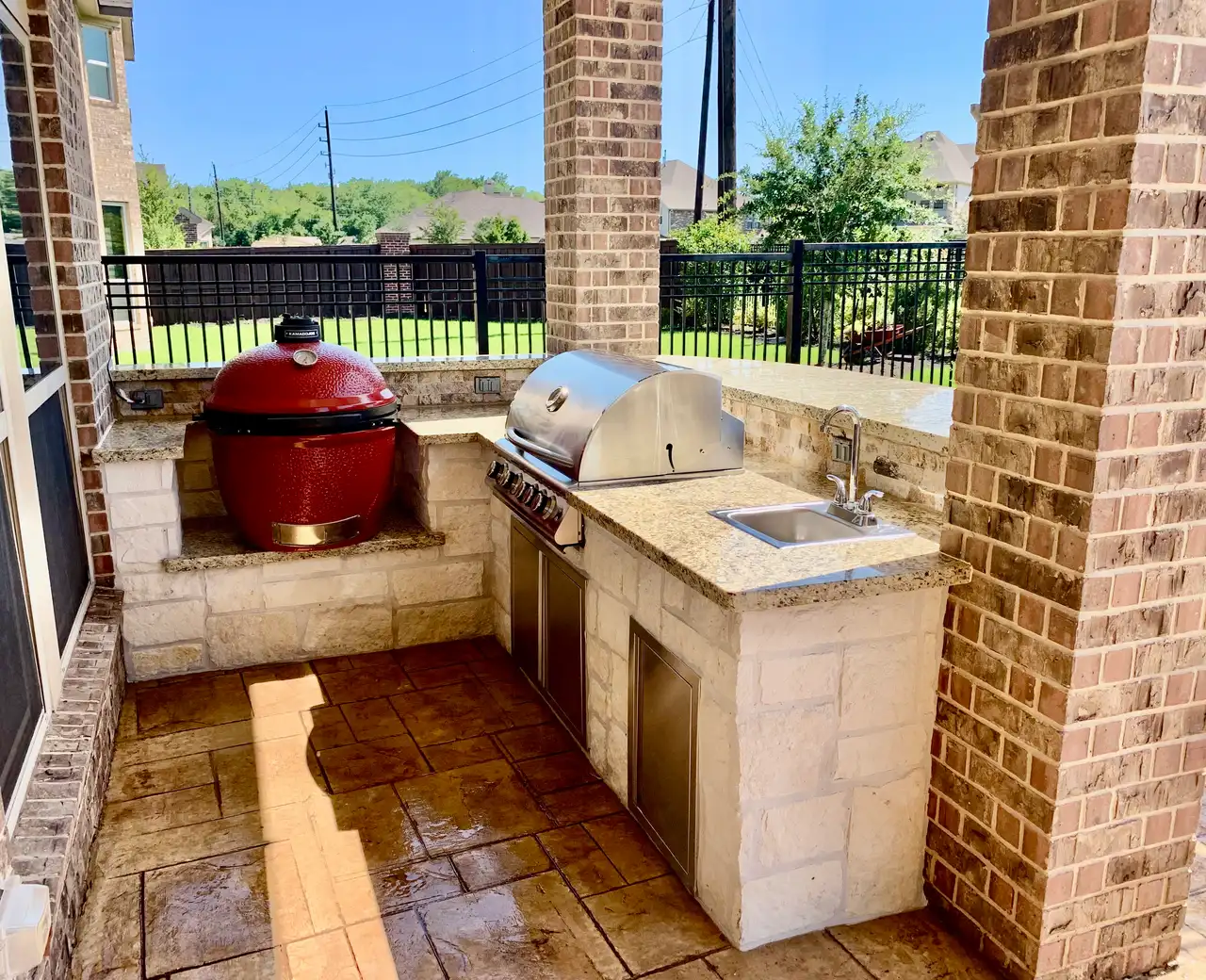 Limestone grill station with a red kamado, stainless grill and sink between brick columns