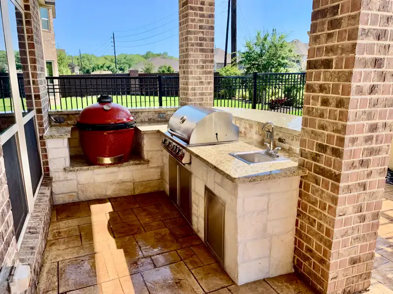 Limestone outdoor grill station with red kamado cooker, stainless grill and sink