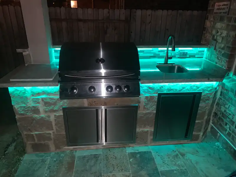 Stone outdoor grill station with LED under-counter lighting and a sink at night