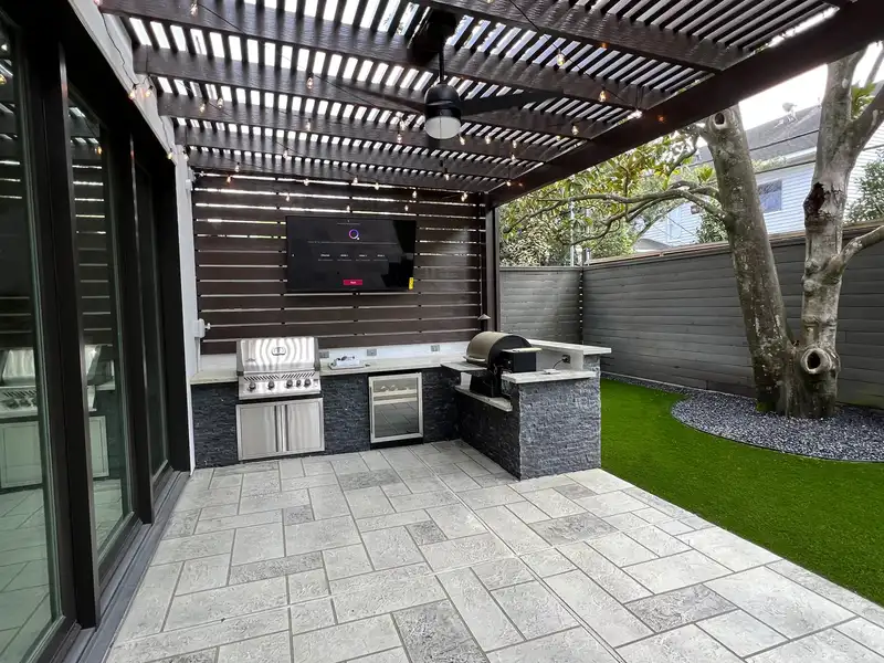 Modern outdoor kitchen under a louvered pergola with a paver patio and artificial turf