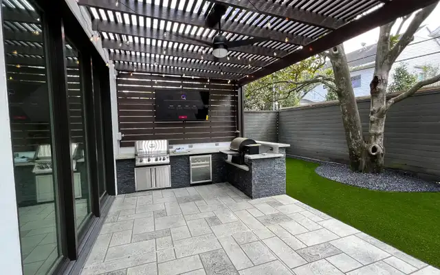 Slatted pergola covering a modern outdoor kitchen with a built-in grill and TV wall