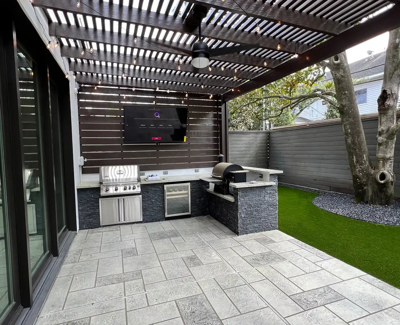 Artificial turf next to a paver patio and modern outdoor kitchen under a louvered pergola