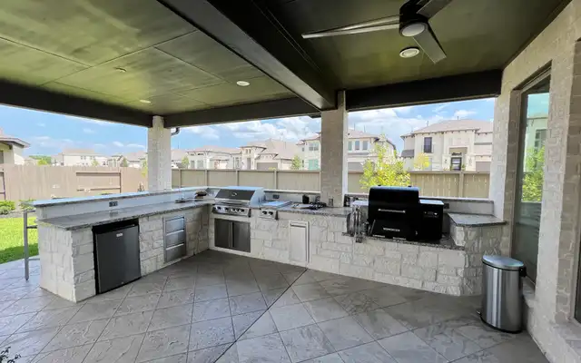 Large L-shaped limestone outdoor kitchen with grill and smoker under a covered patio