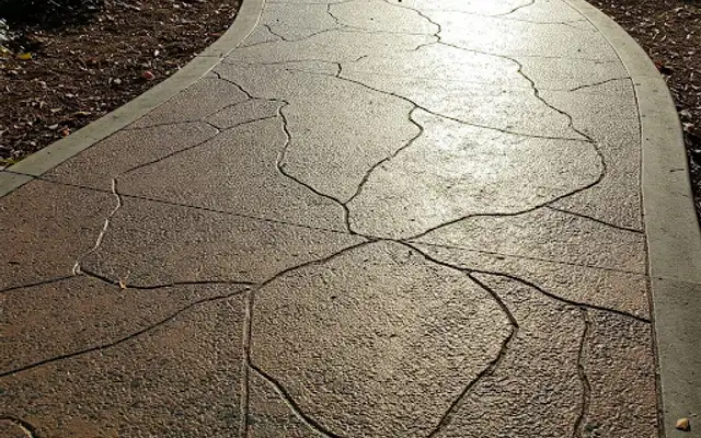 Curving stamped concrete walkway with a flagstone pattern through mulched beds