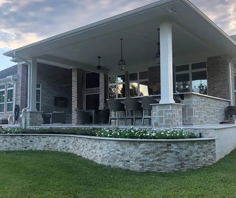 Curved stone planter bed with white flowers below a large covered patio at sunset
