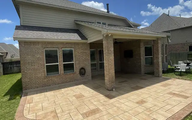 Stamped concrete patio with an ashlar pattern and contrasting border off a covered porch in a Houston backyard