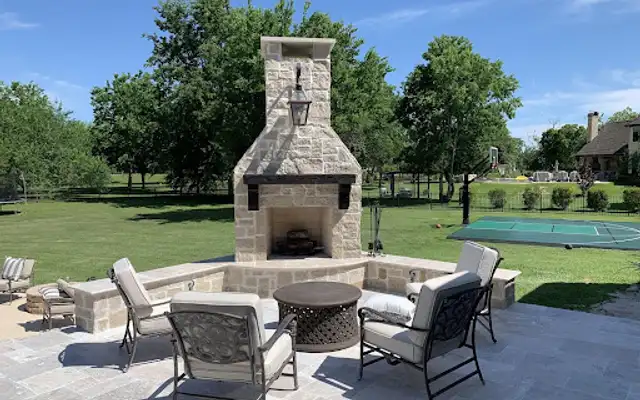 Travertine patio with an outdoor fireplace, stone seat walls and cushioned chairs in a Houston backyard