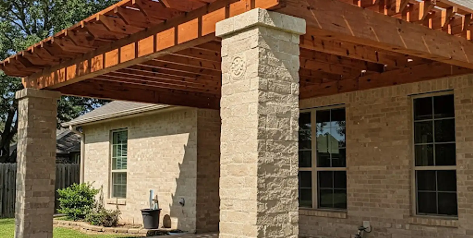 Stained cedar pergola on stone-clad columns over a patio behind a brick home