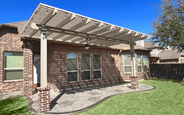 Painted pergola on brick columns over a stamped concrete patio beside a lawn