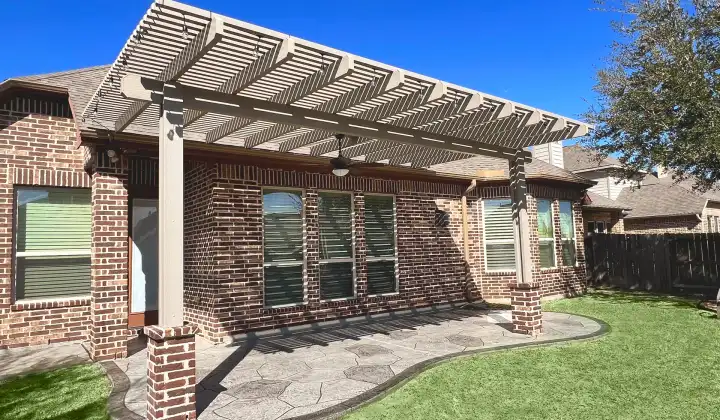 Painted pergola on brick columns over a stamped concrete patio with artificial turf
