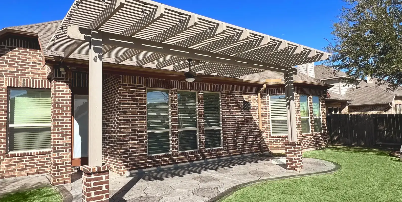 Painted pergola on brick columns over a stamped concrete patio with artificial turf