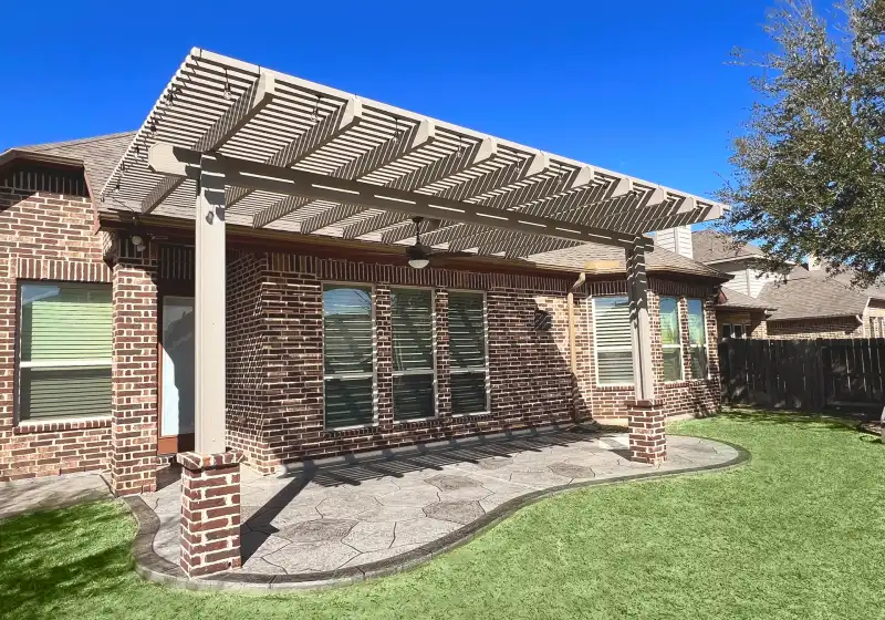 Painted pergola on brick columns over a stamped concrete patio with artificial turf