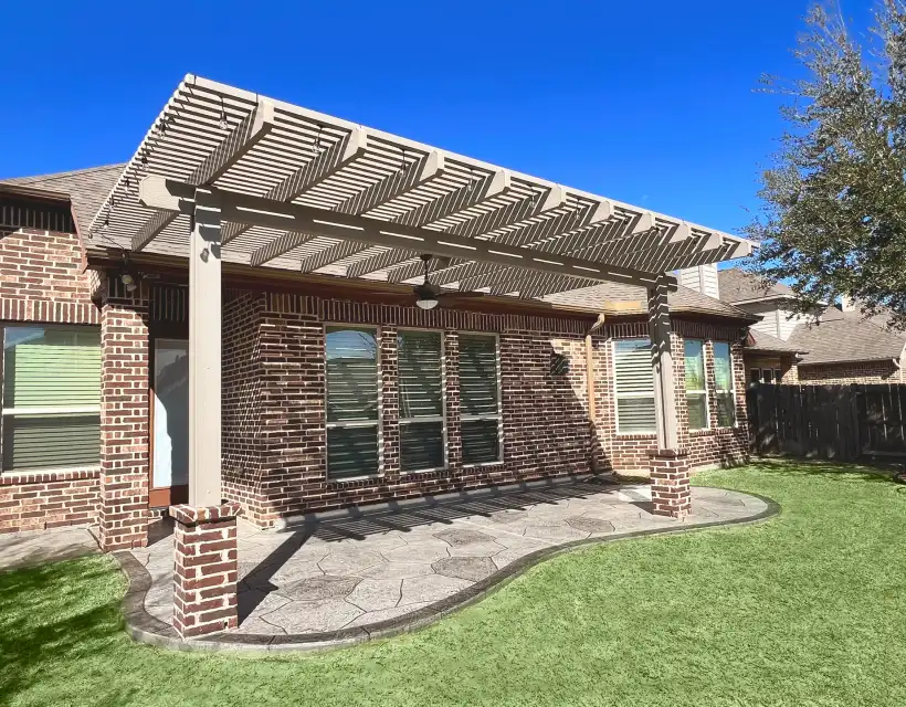 Painted pergola on brick columns shading a stamped concrete patio behind a brick home