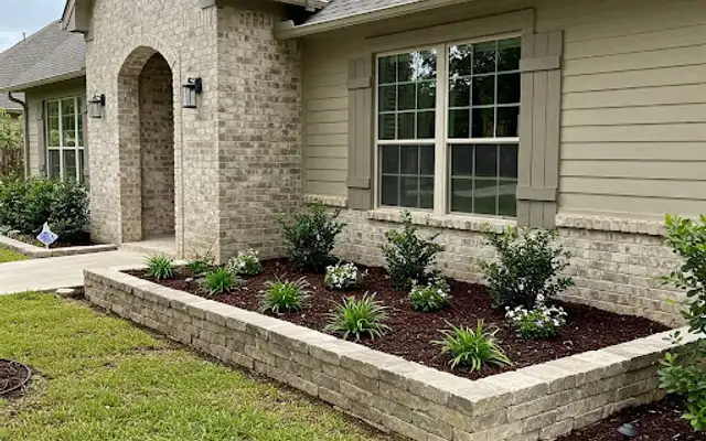 Raised block planter bed with fresh mulch and new shrubs along the front of a house