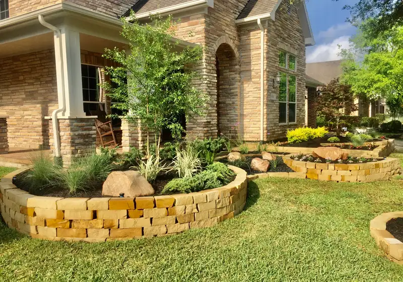Stacked stone raised planting beds with boulders and ornamental grasses at a Houston home