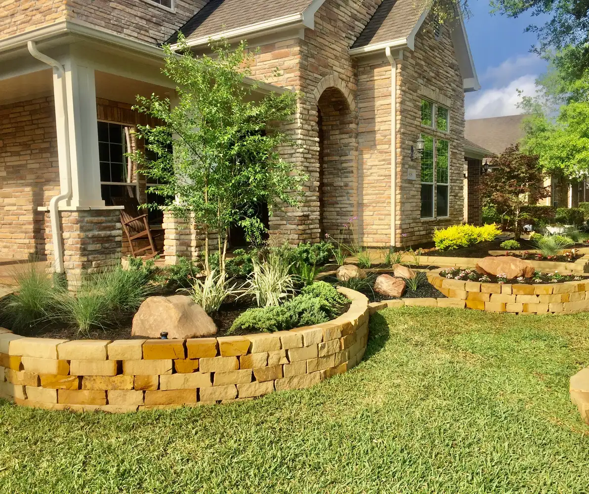 Stacked stone raised planting beds with boulders, grasses and a young tree at a Houston home