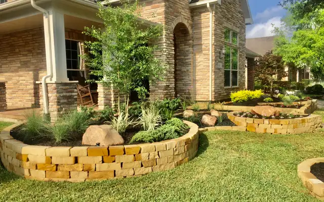 Front yard raised stone planter beds with boulders, ornamental grasses, shrubs and a young tree