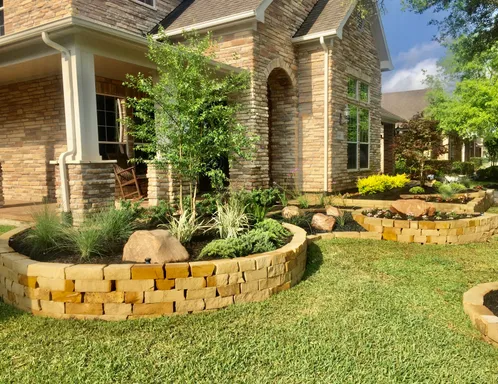 Stacked stone raised planting beds with boulders and ornamental grasses at a Houston home