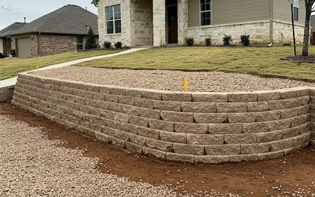 Tan block retaining wall with gravel drainage backfill in front of a new house