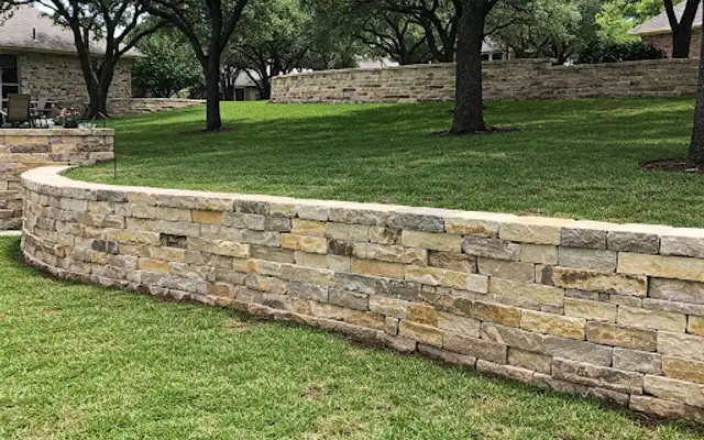 Curving natural limestone retaining wall across a sloped lawn under oak trees