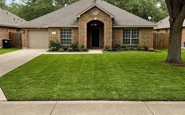 Brick home with a freshly installed sod lawn and a mature oak tree