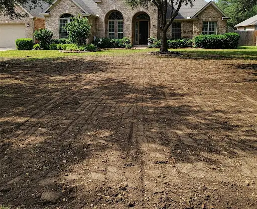Front yard stripped to bare, graded soil and ready for new sod in front of a brick house