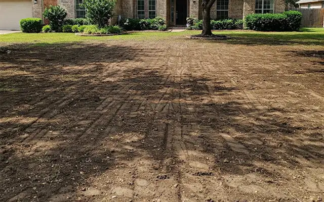 Front yard stripped to bare, graded soil in front of a brick house before new sod
