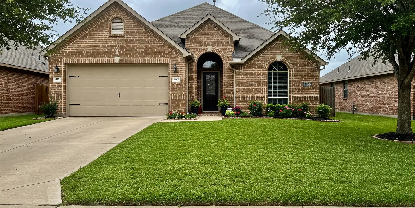 Brick home with a lush green front lawn and potted flowers at the entry