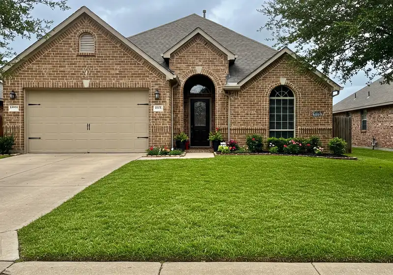 Brick home with a lush green front lawn and potted flowers at the entry